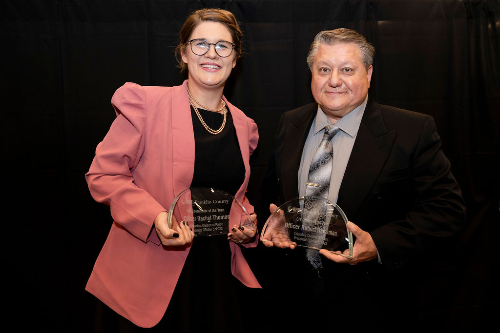 Two people holding up awards in front of a black background.