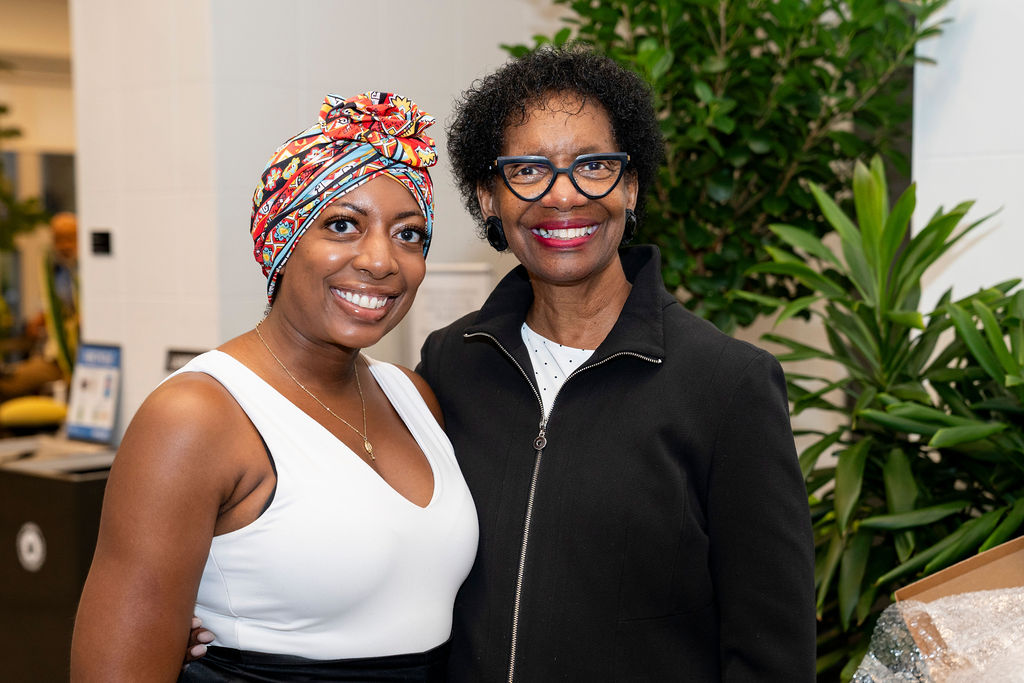 Two women standing next to each other in front of a plant.