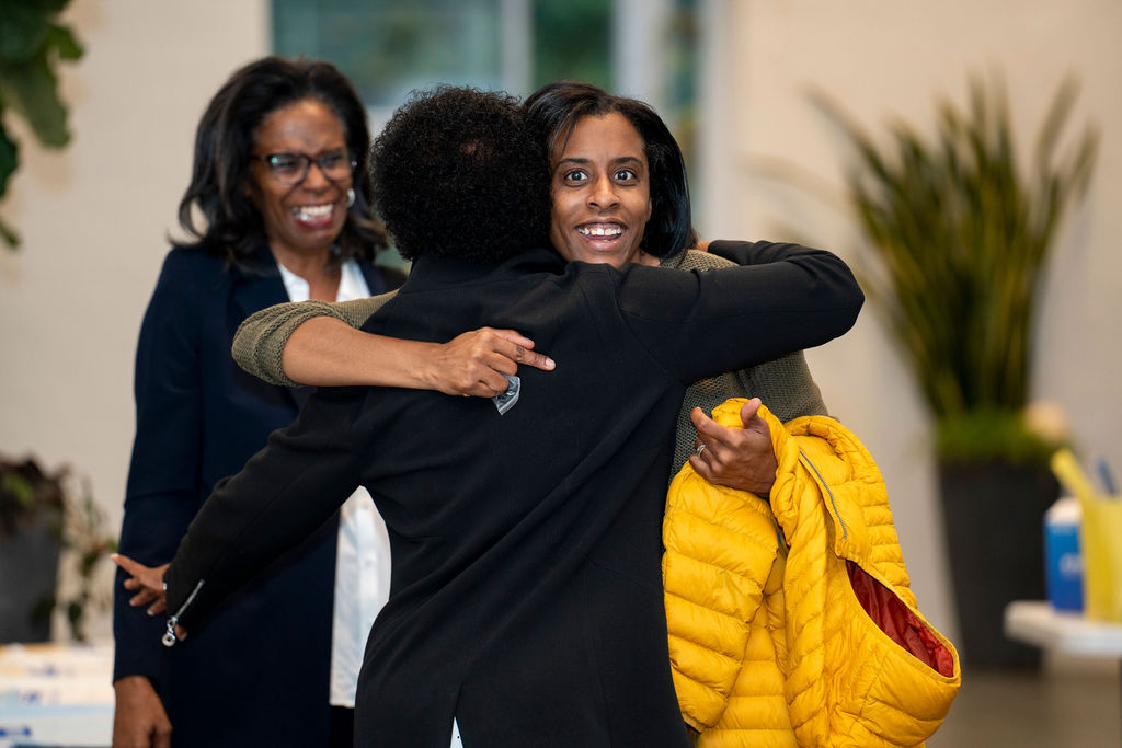 Two women hug each other while another woman looks on.